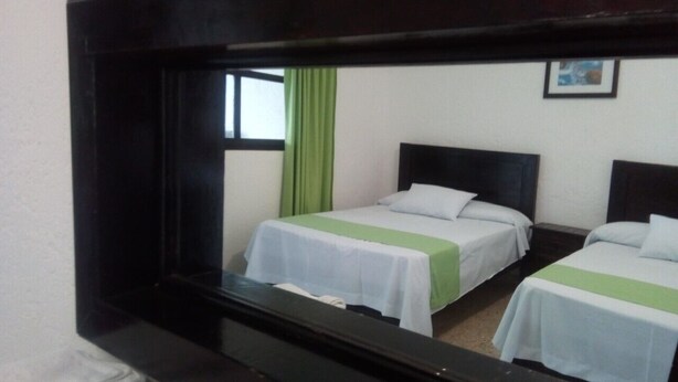 A room with two beds, each with a white and green bedspread, and a mirror reflecting the room. - Hotel D lina Princess suites (San Cristóbal de las Casas)