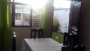A dining area with a table and four chairs, a window with curtains, and a view of a building and greenery outside. - Hotel D lina Princess suites (San Cristóbal de las Casas)