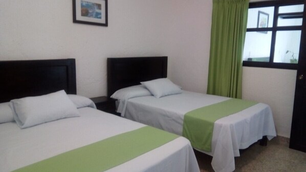Two single beds with white and green bedspreads, a dark headboard, a green curtain, and a window with a view.