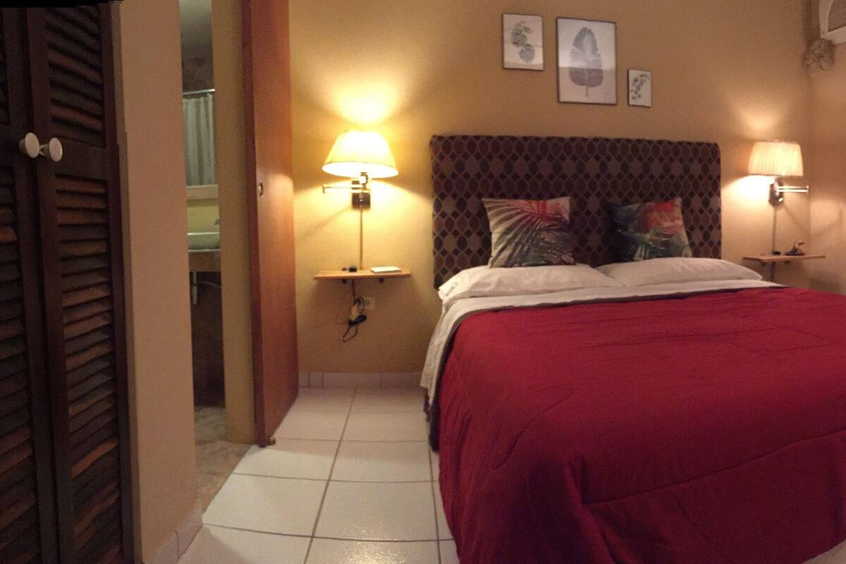 A hotel room with a bed, two bedside lamps, a nightstand, a small cabinet, and a wall-mounted TV.