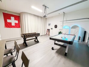 A room with a foosball table, a pool table, and a flag on the wall.