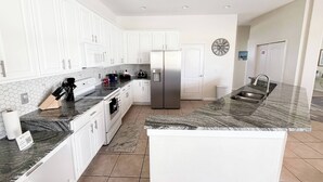 A modern kitchen with white cabinets, a stainless steel refrigerator, a marble countertop, and a large island with a sink. - Stunning Renovated Villa Overlooking Golf Course (Davenport)