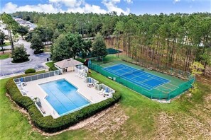 A residential property with a swimming pool, tennis court, and a covered patio area.