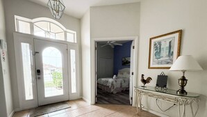 A hallway with a door leading to a bedroom, a glass console table with a lamp, and a framed picture on the wall. - Stunning Renovated Villa Overlooking Golf Course (Davenport)