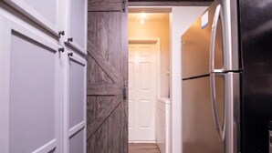 Une cuisine avec un réfrigérateur noir, des armoires blanches et une porte en bois.