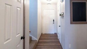 Un couloir avec une porte blanche au fond, un luminaire au plafond et une petite étagère fixée au mur, sur laquelle sont posés quelques objets.