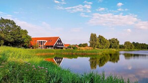 Un'azienda agricola tradizionale olandese con un ampio fienile, uno stagno e vegetazione circostante.