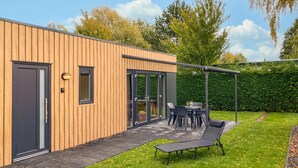 Una casa moderna con facciata in legno, un patio con tavolo e sedie, un'amaca e una zona relax coperta.