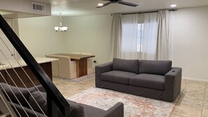 A modern living room with a gray sofa, a dining table, and a staircase.