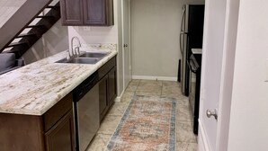A compact kitchen with dark wooden cabinets, a white marble countertop, and a built-in dishwasher.