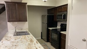 A kitchen with a granite countertop, stainless steel appliances, and dark wooden cabinets.