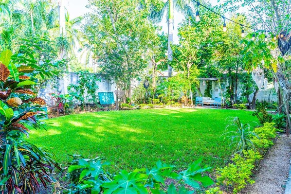 A lush garden with a variety of plants and trees, a grassy lawn, and a seating area with a bench and table.