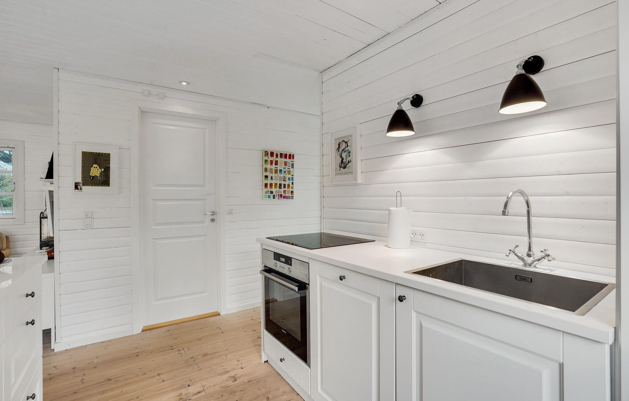 A modern kitchen with white cabinetry, a built-in oven, a sink with a faucet, and pendant lighting.