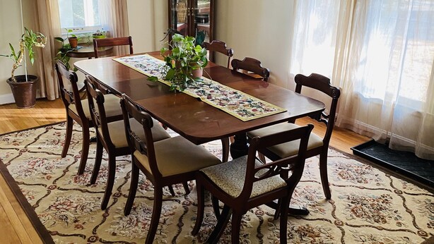 Un comedor con una mesa de madera, seis sillas, un tapete floral y plantas en macetas.