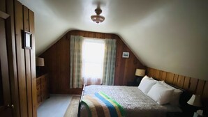 Un dormitorio con cama, ventana con cortinas, ventilador de techo y paredes de madera.