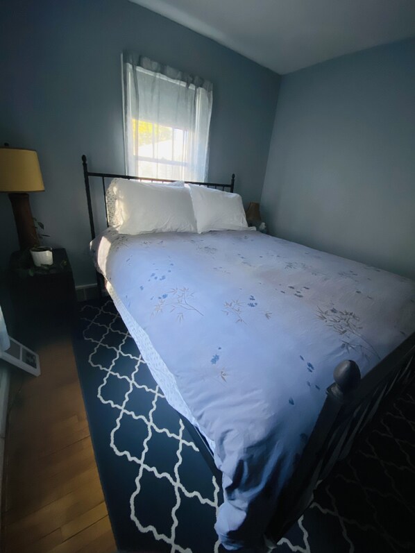 Un dormitorio con cama, mesita de noche, lámpara y ventana con cortinas.