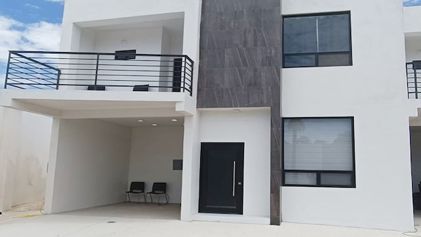 Un edificio moderno de dos pisos con un balcón, una puerta negra y dos ventanas.