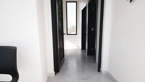 Un pasillo con paredes blancas y suelo de baldosas que conduce a una puerta con ventana.