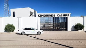 Un coche blanco estacionado frente a una entrada con puerta y el letrero "CONDOMINIOS CASAMAR".