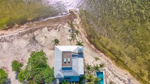 Vista aérea de una propiedad frente a la playa con piscina, palmeras y una vista despejada del océano.