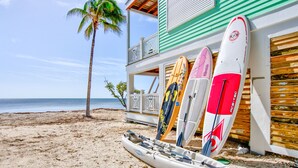 Una playa con una fila de tablas de surf apoyadas contra un edificio.