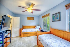 Une chambre à coucher avec deux lits en bois, un ventilateur de plafond, une télévision et une fenêtre donnant sur un paysage verdoyant.