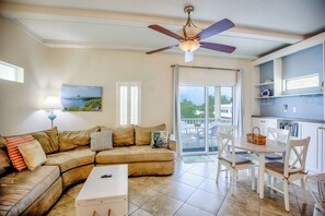 Relax in this open-plan living space with a curved sofa, dining area, and kitchen, offering a view of lush greenery from the balcony.