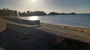 Una playa con cielo despejado, mar tranquilo y colinas al fondo.