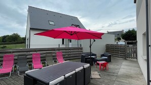 Terraza al aire libre con zona de comedor, que incluye una mesa y sillas, y un gran paraguas rosa.