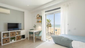 Ein modernes Hotelzimmer mit Fernseher, Schreibtisch, Bett und einem Balkon mit Blick auf den Strand.