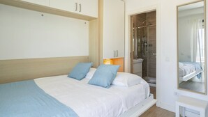 Ein Schlafzimmer mit Bett, bodenebener Dusche und großem Spiegel.