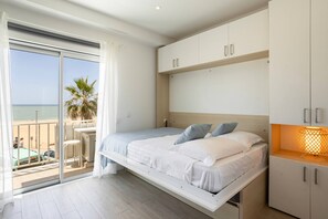 A bedroom with a bed, a nightstand, a lamp, a sliding door to a balcony, and a view of the beach. - Beach Front Studio w/Premium View -Astro Quarteira (Loulé)