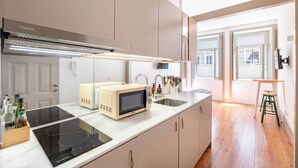 Una cocina moderna con microondas integrado, estufa y lavaplatos. Hay un taburete de madera y una ventana con vistas a la ciudad.