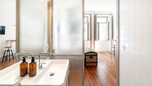 Un baño moderno con un lavamanos grande, dos dispensadores de jabón, un taburete y un banco.