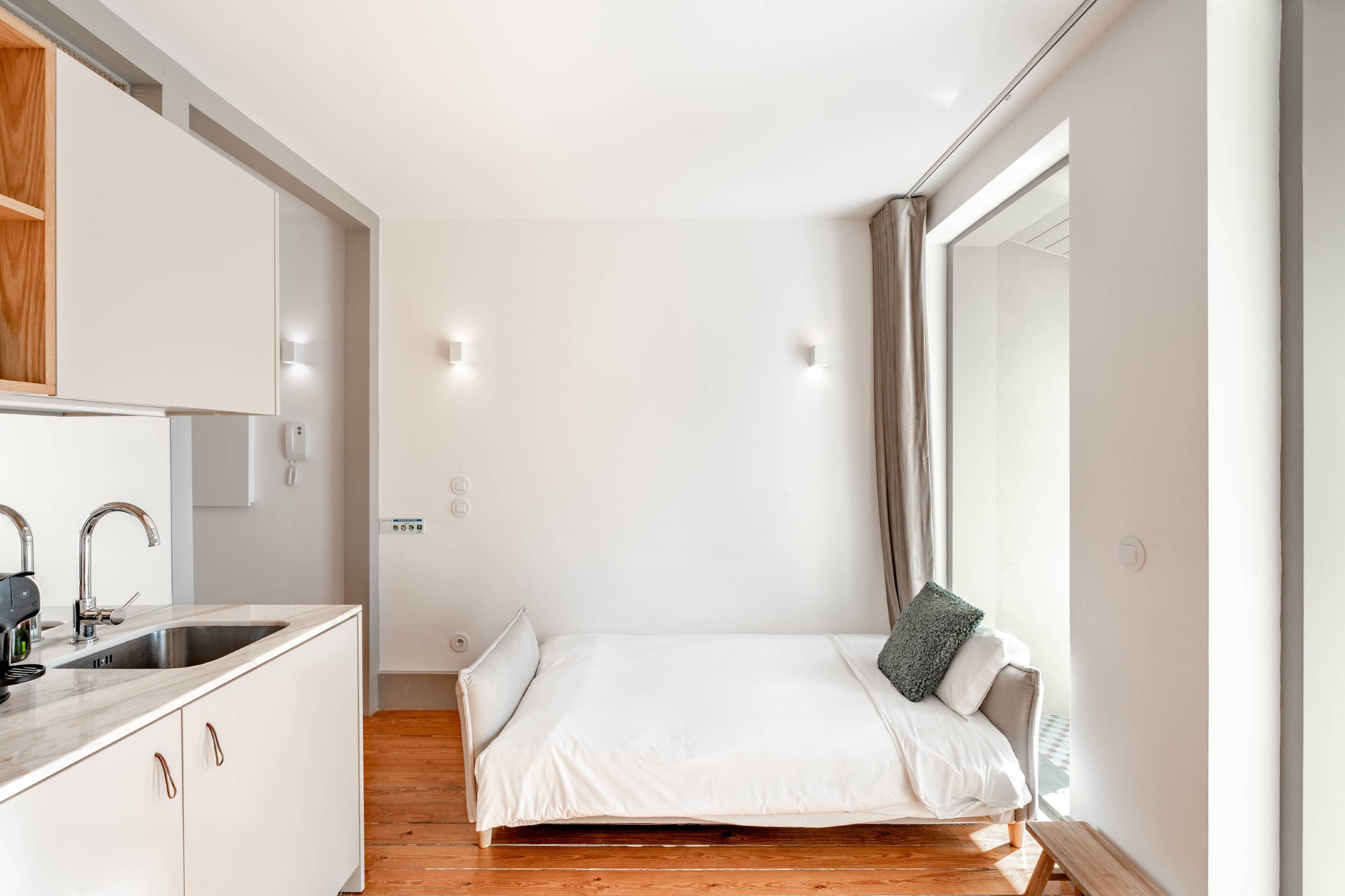 A compact bedroom with a bed, a small bedside table, a built-in wardrobe, and a window with curtains.