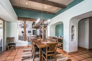 A spacious dining area with a wooden table and chairs, a chandelier, and a tiled floor.
