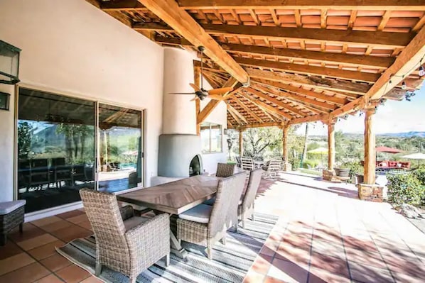 An outdoor patio with a wooden pergola, wicker furniture, and a view of the surrounding landscape.