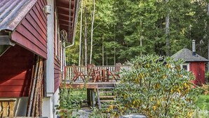 Ein rotes Holzhaus mit Veranda, einem kleinen Schuppen und einem Grill im Vordergrund.