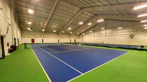 An indoor tennis court with a green and blue playing surface, surrounded by walls and a high ceiling with lighting fixtures.