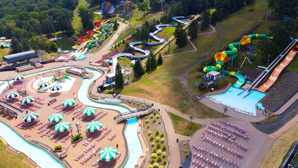 An aerial view of a water park with multiple slides and pools, surrounded by trees and a picnic area.