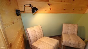 Een kamer met houten lambrisering, twee gestreepte stoelen en een wandlamp.