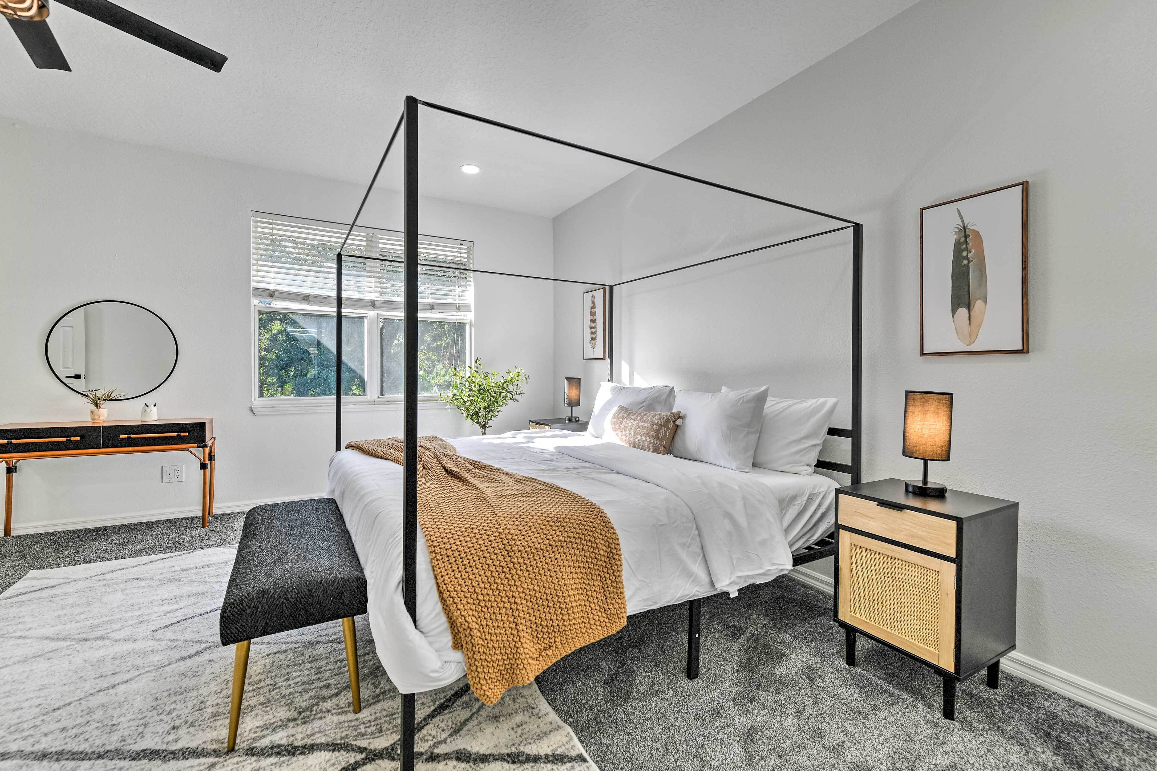 A modern bedroom with a four-poster bed, bedside tables, a bench, and a window with blinds.