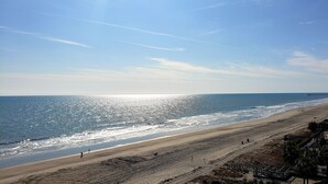 A beach with a clear sky, a pier in the distance, and a building adjacent to the beach. - Newly Renovated Beachfront Oasis. (Myrtle Beach)