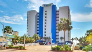 A multi-story hotel with a prominent blue and white facade, a sign indicating it is Ocean Park, and a parking lot with several cars. - Newly Renovated Beachfront Oasis. (Myrtle Beach)