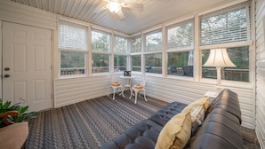 Una veranda con ventilatore a soffitto, ampie finestre, un divano nero e un tappeto decorato.
