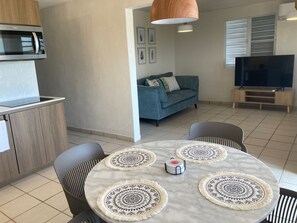 A modern living room with a round marble table, two armchairs, a sofa, a television, and a kitchen area with a microwave.