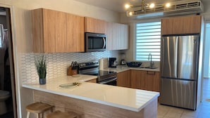 A modern kitchen with wooden cabinets, a stainless steel refrigerator, a microwave, and a large island with stools. - Walking distance to Boqueron, private pool, full A/C, sleeps 10 (Boquerón)