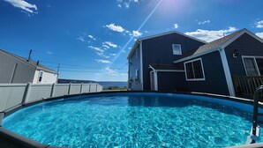 Una piscina con agua azul cristalina, rodeada por una terraza de madera y una casa con fachada oscura.
