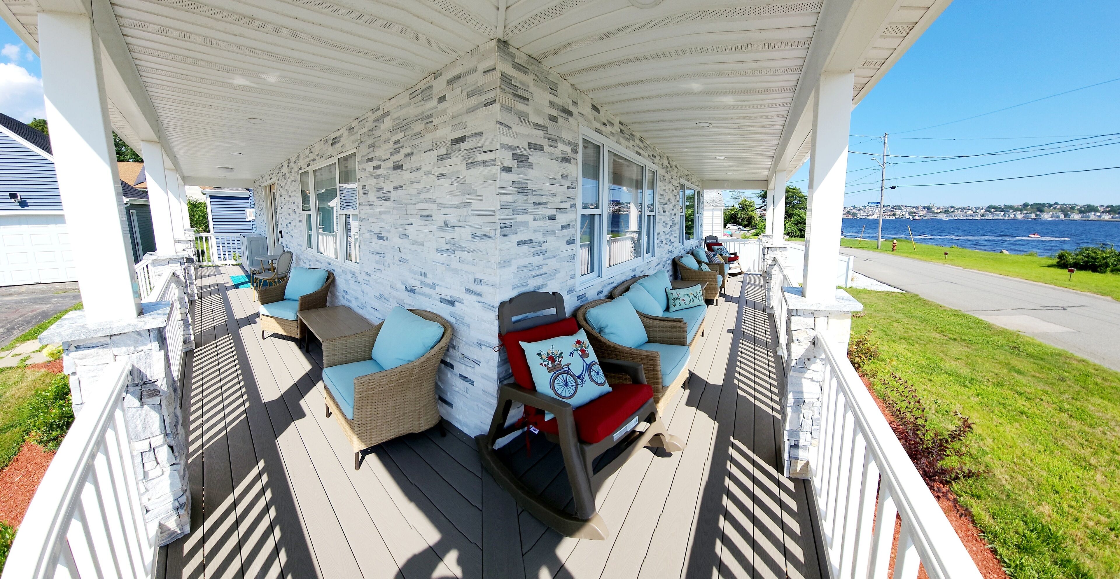 Een overdekt terras met buitenmeubilair, een stenen muur en uitzicht op het water.