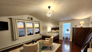 Un dormitorio con una ventana grande, una cama, un escritorio, una silla y un aparador.